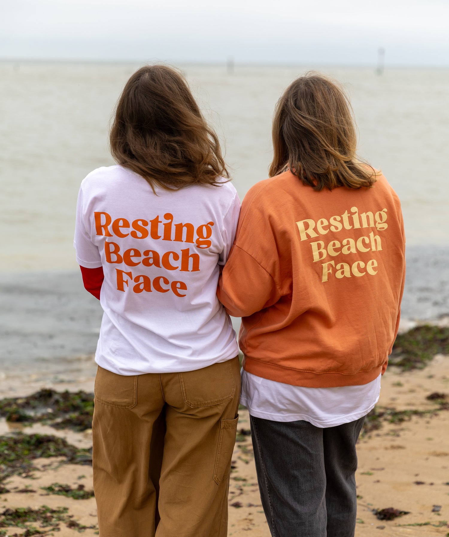 Two people standing on a beach with 'Resting Beach Face' shirts.