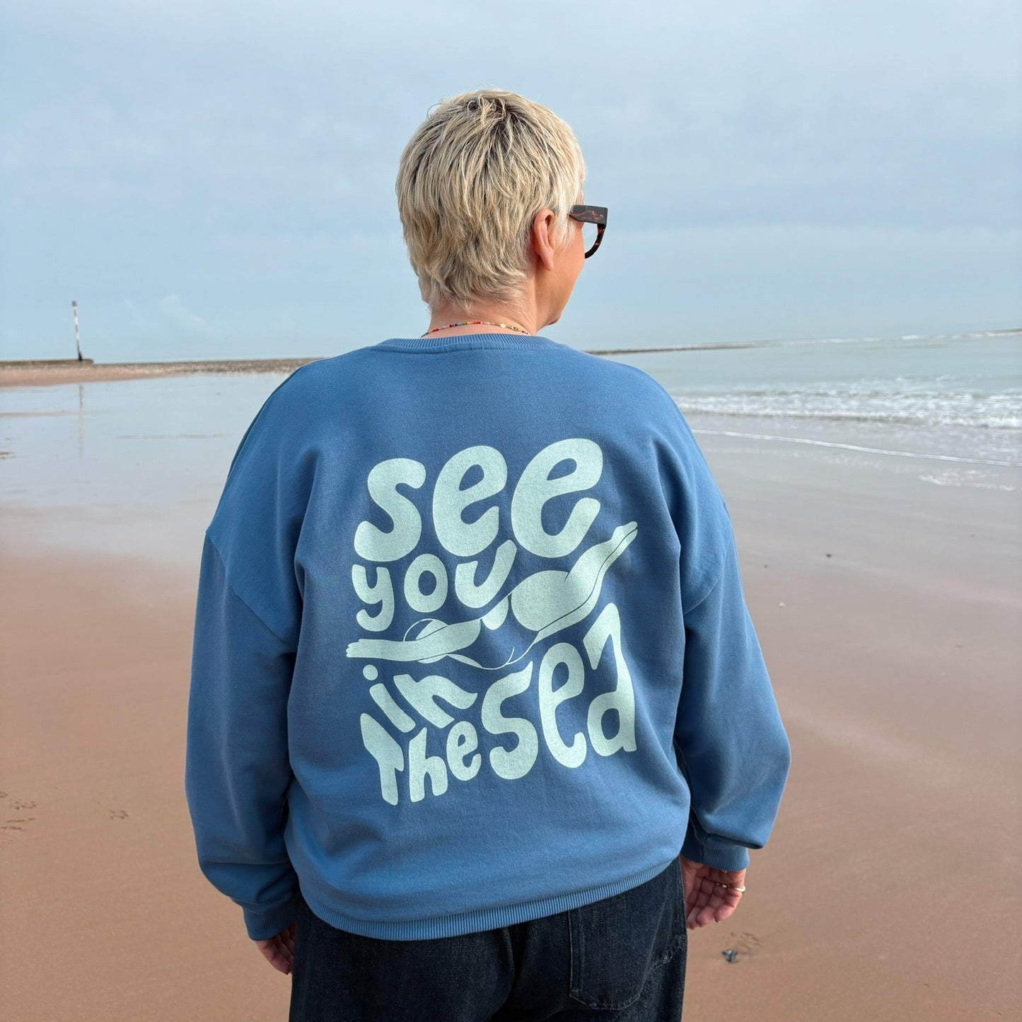 Person wearing a blue sweatshirt with text on the beach